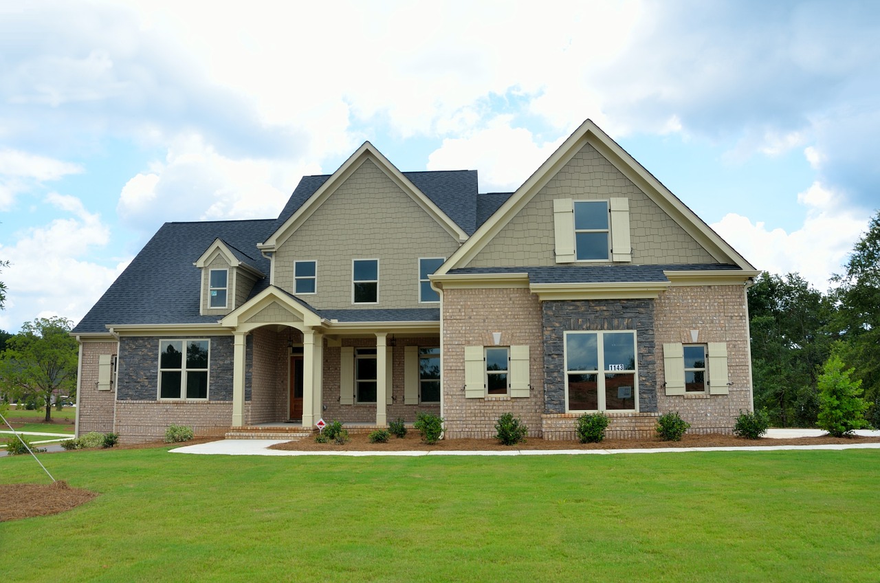 A modern two-story house featuring a brick and siding exterior, front porch, and large windows, surrounded by a grassy lawn.